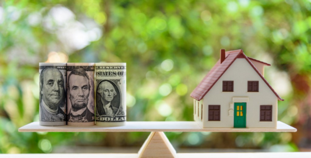Home loan / reverse mortgage or transforming assets into cash concept : House model, US dollar notes on a simple balance scale, depicts a homeowner or a borrower turns properties / residence into cash